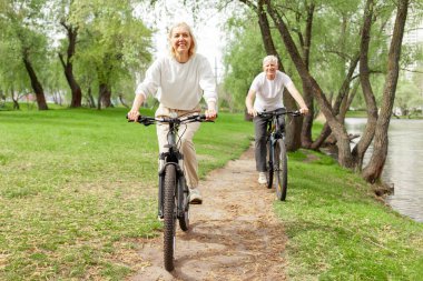 Yaşlı yaşlı çift yazın parkta bisiklete biniyor ve gülümsüyor, yaşlı beyaz saçlı adam ve kadın dışarıda dinleniyor, yaşlı insanlar ormanda bisiklet pratiği yapıyor.