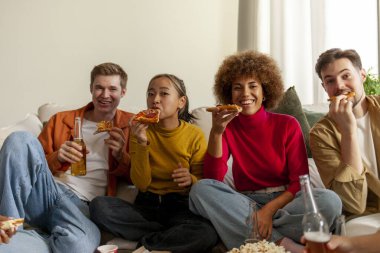 Ev partisinde pizza yiyen, bira içen ve arkadaşlarıyla eğlenen farklı etnik kökenli bir grup genç bir evde alkol içip fast food yiyorlar.