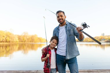 Afrika kökenli Amerikalı bir adam ve çocuk ellerinde oltalarla nehirde tahta iskelede duruyorlar, baba oğluna gölde balık tutmayı öğretiyor, aile hafta sonları dinleniyor ve dinleniyor.