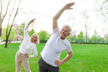 Yaşlı bir çift yaşlı erkek ve kadın parkta egzersiz yapıyor ve antrenman yapıyor, kır saçlı büyükanne ve büyükbaba spor yapıyor ve doğada aktif bir yaşam sürüyor.