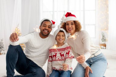 Noel Baba şapkalı Afro-Amerikan ailesi yılbaşını birlikte kutluyor ve Noel ağacının yanında evde maytap tutuyor, anne baba ve küçük oğlu Noel 'de eğleniyor.