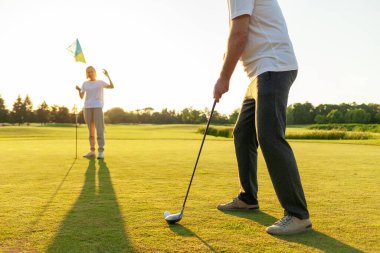 Yaşlı çiftler golf sahasında gün batımında golf oynuyorlar, yaşlı adam ve kadın golf sopalarıyla pratik yapıyorlar, beyaz üniformalı karı koca aktif olarak dinleniyorlar.