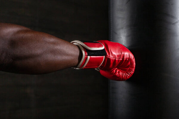 Крупный план афроамериканских боксеров в красной перчатке, бьющих грушу для битья. Мышцы напряжены, передавая силу и точность удара в темном зале