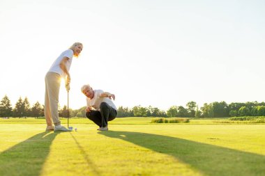 Golf sahasında golf oynayan yaşlı bir çift yaşlı bir adam, kadınlara golf sopası ve salıncak topunu nasıl tutacağını öğreten yaşlı bir öğretmen, büyükannenin dışarıda oynamasına yardım eden büyükbaba.