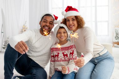 Noel Baba şapkalı Afro-Amerikan ailesi yılbaşını birlikte kutluyor ve Noel ağacının yanında evde maytap tutuyor, anne baba ve küçük oğlu Noel 'de eğleniyor.