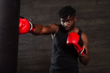 Kırmızı eldiven giyen güçlü Afrikalı Amerikalı boksör spor salonunda kum torbasına vurmaya hazırlanıyor. Boks müsabakasından önce atlet trenleri ve kararlılığını gösteriyor.