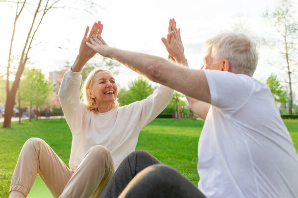 elderly couple of seniors man and woman high-five and rejoice at success in the park outdoors, gray-haired grandparents celebrate victory and play sports in nature