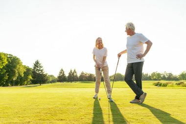 ... golf sahasında golf oynayan yaşlı bir adam ve bir kadın gün batımında golf oynayan yaşlı bir çift aktif olarak dışarıda eğleniyor ve spor yapıyor.