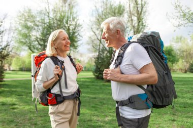 Yaşlı atletik bir çift yaşlı erkek ve kadın yürüyüş sırt çantalarıyla ormanda geziyorlar, kır saçlı büyükanne ve büyükbaba doğa yürüyüşüne çıkıyorlar.