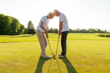Spor giyim sektöründe yaşlı bir çift golf oynuyor. Yeşil bir araziye başları dokunup topa vurarak dururlar. Parlak güneş atmosfere katıyor