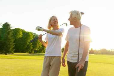 Yaşlı çift golf sahasında golf oynuyor ve gün batımında sohbet ediyor. Yaşlı erkek ve kadın dışarıda dinleniyor ve gülüyor. Emekliler tatilde.