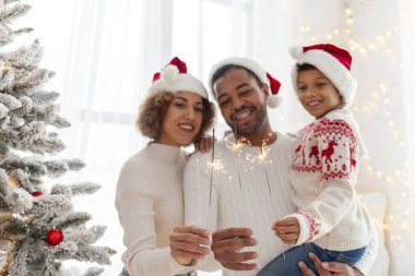Noel Baba şapkalı Afro-Amerikan ailesi yılbaşını birlikte kutluyor ve Noel ağacının yanında evde maytap tutuyor, anne baba ve küçük oğlu Noel 'de eğleniyor.