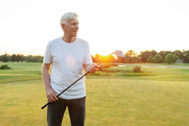 Gri saçlı, golf oynayan ve golf kulübünü elinde tutan yaşlı bir adam. Kıdemli işadamı gün batımında spor yapıyor ve dinleniyor.