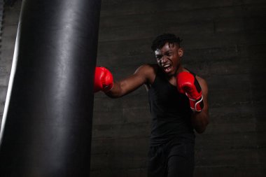 Yüzünde öfkeli bir ifadeyle Afrika kökenli Amerikalı bir boksör karanlık bir spor salonundaki kum torbasına güçlü bir yumruk indiriyor. Rakibini mağlup etmek için gücünü ve kararlılığını gösteriyor.