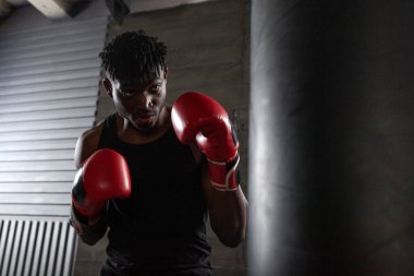 Kırmızı eldivenli güçlü bir Afrikalı Amerikalı boksör spor salonunda yumruğa hazırlanıyor. Kararlılığını ve gücünü gösteriyor..
