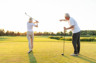 Golf sahasında golf oynayan yaşlı bir çift yaşlı bir adam, kadınlara golf sopası ve salıncak topunu nasıl tutacağını öğreten yaşlı bir öğretmen, büyükannenin dışarıda oynamasına yardım eden büyükbaba.