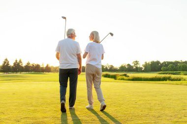 Üniformalı yaşlı bir çift ellerinde golf sopalarıyla gün batımında golf sahasında yürüyorlar ve konuşuyorlar. Yaşlı adam ve kadın golf oynayıp konuşuyor ve fotokopi alanına bakıyorlar.