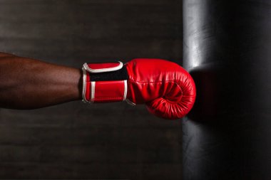 boxer hand in red glove hitting punching bag on black background, african american athlete training punch, close up clipart