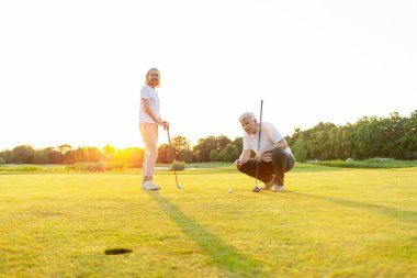 Golf sahasında golf oynayan yaşlı bir çift yaşlı bir adam, kadınlara golf sopası ve salıncak topunu nasıl tutacağını öğreten yaşlı bir öğretmen, büyükannenin dışarıda oynamasına yardım eden büyükbaba.