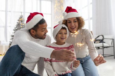 Noel Baba şapkalı Afro-Amerikan ailesi yılbaşını birlikte kutluyor ve Noel ağacının yanında evde maytap tutuyor, anne baba ve küçük oğlu Noel 'de eğleniyor.
