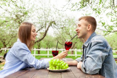 Kot elbiseli genç bir çift, tahta bir masada oturmuş, yazın bir randevuda üzümlü kırmızı şarap içiyorlar, erkek ve kız alkollü kokteyller deniyor ve flört ediyorlar.