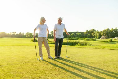 Yaşlı çift golf sahasında golf oynuyor ve gün batımında sohbet ediyor. Yaşlı erkek ve kadın dışarıda dinleniyor ve gülüyor. Emekliler tatilde.