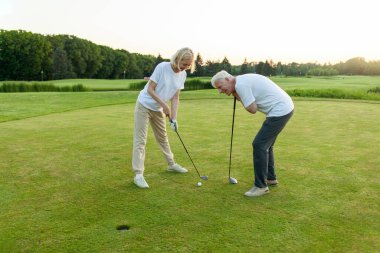 Yaşlı çift golf sahasında golf oynuyor ve gün batımında sohbet ediyor. Yaşlı erkek ve kadın dışarıda dinleniyor ve gülüyor. Emekliler tatilde.