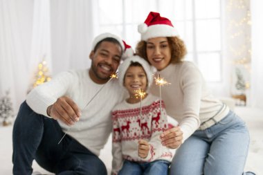 Noel Baba şapkalı Afro-Amerikan ailesi yılbaşını birlikte kutluyor ve Noel ağacının yanında evde maytap tutuyor, anne baba ve küçük oğlu Noel 'de eğleniyor.