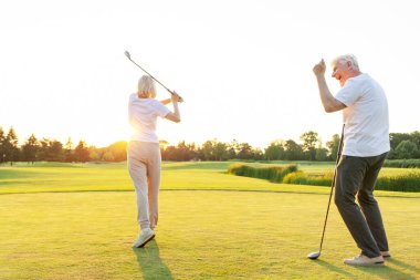 Yaşlı çift golf sahasında golf oynuyor ve gün batımında sohbet ediyor. Yaşlı erkek ve kadın dışarıda dinleniyor ve gülüyor. Emekliler tatilde.