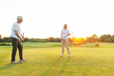 ... golf sahasında golf oynayan yaşlı bir adam ve bir kadın gün batımında golf oynayan yaşlı bir çift aktif olarak dışarıda eğleniyor ve spor yapıyor.