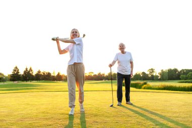 Yaşlı çift golf sahasında golf oynuyor ve gün batımında sohbet ediyor. Yaşlı erkek ve kadın dışarıda dinleniyor ve gülüyor. Emekliler tatilde.