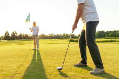 Yaşlı çift golf sahasında golf oynuyor ve gün batımında sohbet ediyor. Yaşlı erkek ve kadın dışarıda dinleniyor ve gülüyor. Emekliler tatilde.