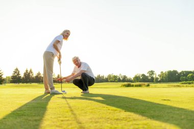 Yaşlı çift golf sahasında golf oynuyor ve gün batımında sohbet ediyor. Yaşlı erkek ve kadın dışarıda dinleniyor ve gülüyor. Emekliler tatilde.