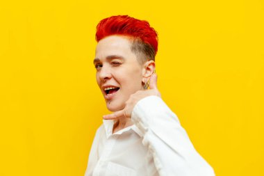 Genç, kısa saçlı, kızıl saçlı kız gösterileri bana jest diyor ve sarı izole arka planda göz kırpıyor. Piercingli hippi bir kadın ve telefonda konuşma sembolü gösteriyor.