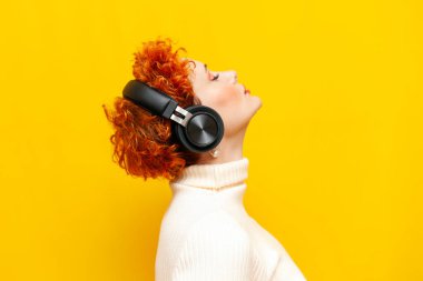 Kıvırcık saçlı genç bir kadın kulaklıkla müzik dinliyor. Gözleri sarı izole arka planda kapalı. Güzel makyajlı bir kız ses altında meditasyon yapıyor ve başını kaldırıyor.