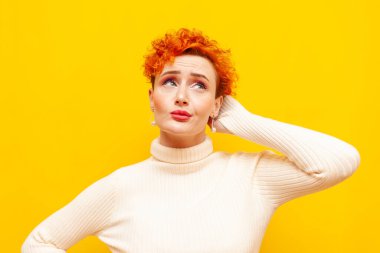 Genç kızıl saçlı, kıvırcık saçlı, belirsiz bir kadın sarı izole bir arka planda düşünür ve hatırlar. Güzel makyajlı kafası karışık bir kız unutur ve merak eder.