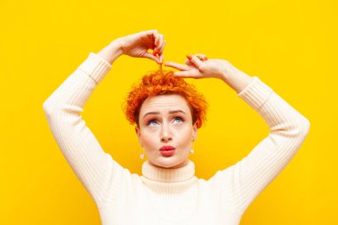 Kıvırcık saçlı genç bir kadın, sarı izole edilmiş arka planda elleri olan makas gösteriyor. Güzel makyajlı bir kız saçını kesip kısa saç kesmek istiyor.