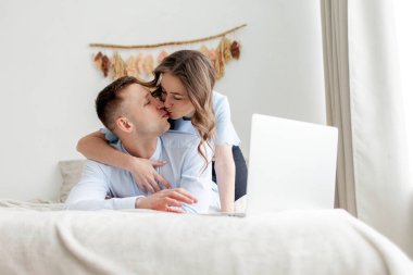 Genç ve mutlu çift evdeki yatakta dizüstü bilgisayar kullanıyor ve öpüşüyorlar. Kadın internette çalışan adama sarılıyor ve film izliyor.