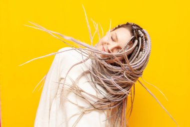 Gri saçlı neşeli bir kız sarı izole bir arka planda saçlarını ve başını sallıyor. Alışılmadık bir saç stili ve örgülü bir kadın dans ediyor ve hareket ediyor.