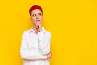 Genç, kısa saçlı, kızıl saçlı, düşünceli kız sarı izole bir arka plan düşünüyor ve planlıyor. Şaşırtıcı hayalleri ve hayalleri olan kafası karışık hippi kadın ve fotokopi alanına bakıyor.