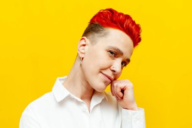 Genç, kısa saçlı, kızıl saçlı bir kız sarı izole bir arka planda kameraya bakar ve düşünür. Piercingli ve renkli saçlı hippi bir kadın.