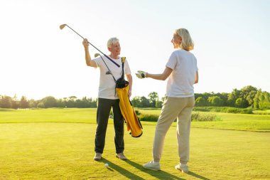 Golf sahasında golf oynayan ve gülümseyen yaşlı yaşlılar, golf sopaları tutan emekli büyükanne ve büyükbabalar ve onları çantaya koyan yaşlı bir adam ve kadın spor yapıyor ve dışarıda antrenman yapıyorlar.
