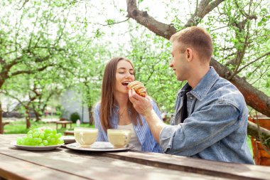 Kot elbiseli, bahçede oturan, kahve içen, yazın randevuda kruvasan yiyen, kız kıza yemek yediren ve terasta flört eden genç bir çift.