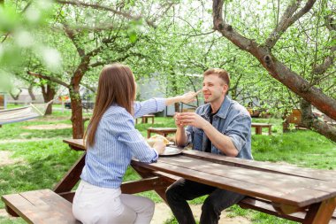 Kot elbiseli genç bir çift ağaçtan bir masanın bahçesinde oturuyor ve yaz mevsiminde konuşuyorlar. Erkek ve kız parkta konuşup flört ediyorlar.