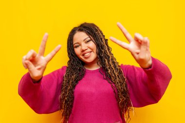 Sarıya boyanmış arka planda barış jesti gösteren, rastalı gülüşlü, tombul Afrikalı Amerikalı kadın artı iki parmaklı, uzun saçlı, uzun boylu bir kız.