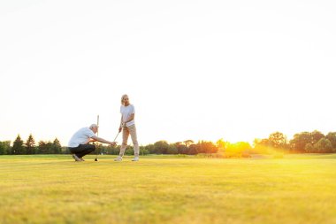 Yaşlı çift golf sahasında golf oynuyor ve gün batımında sohbet ediyor. Yaşlı erkek ve kadın dışarıda dinleniyor ve gülüyor. Emekliler tatilde.