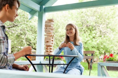 Çocuklar bahçede masa eğitimi oyunu oynuyorlar, kız ve erkek çocuklar tahta bloklar ve gülücüklerle kule inşa ediyorlar, kız ve erkek kardeşler parkta Jenga 'da yarışıyorlar.