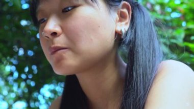 Genç, neşeli Asyalı kadın dışarıda yemek çubuklarıyla pilav yiyor ve seviniyor. Parktaki restoranda öğle yemeği yiyor ve Asya yemeklerini seviyor. Yakın plan.