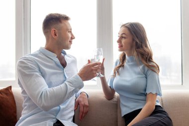 Genç aşıklar bardaklarını beyaz şarapla doldurup evdeki kanepede kutlama yapıyorlar. Kız ve erkek dairede şampanya içip rahatlıyorlar.