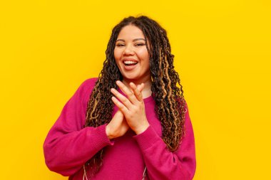 Saçları örgülü neşeli, tombul Afro-Amerikan kadın alkışlar ve sarı izole bir arka planda kameraya bakar. Rasta bukleli iri yarı bir kız ellerini alkışlar ve alkışlar.